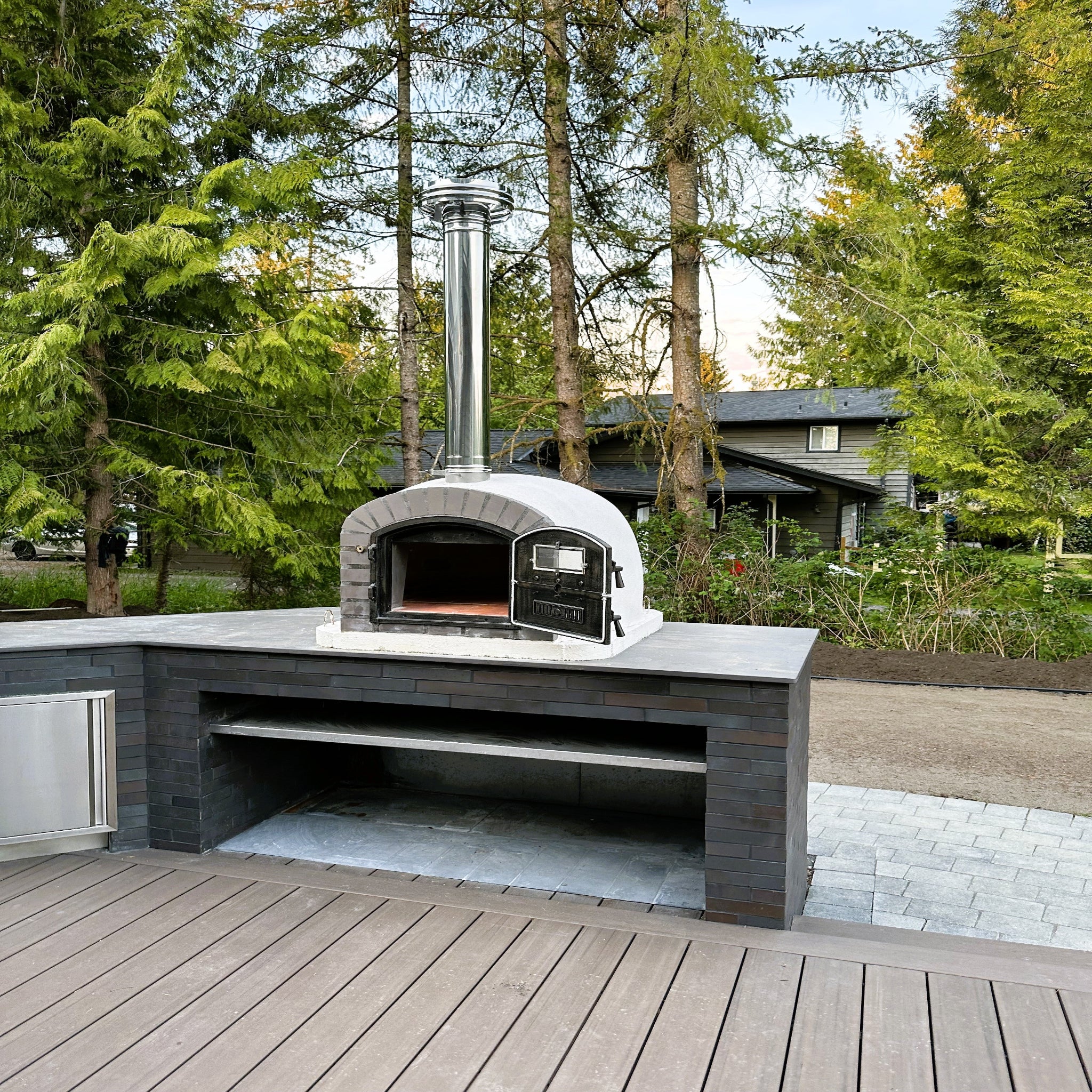 Outdoor pizza oven on a wooden deck with trees in the background