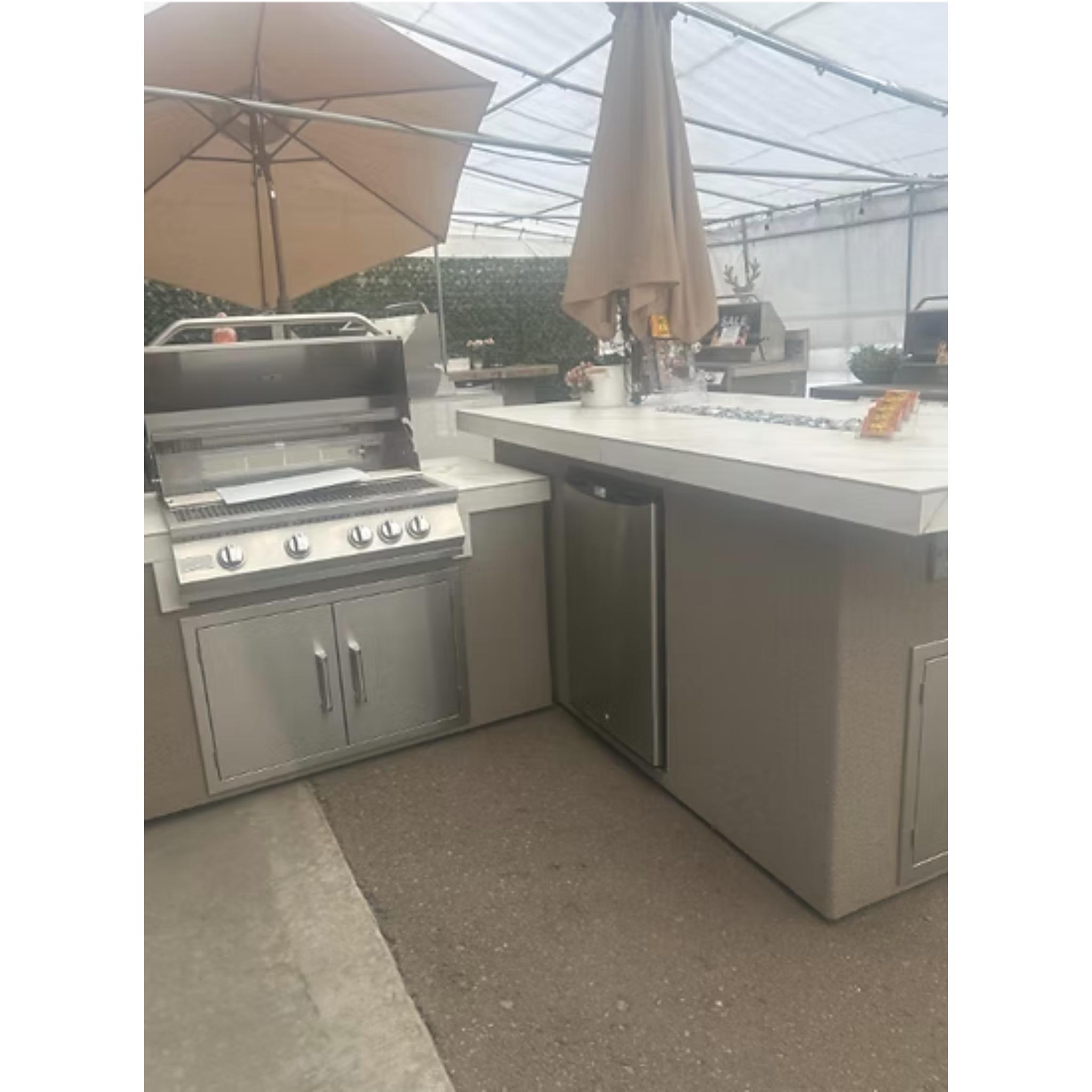 Outdoor kitchen with stainless steel grill and refrigerator under a clear roof