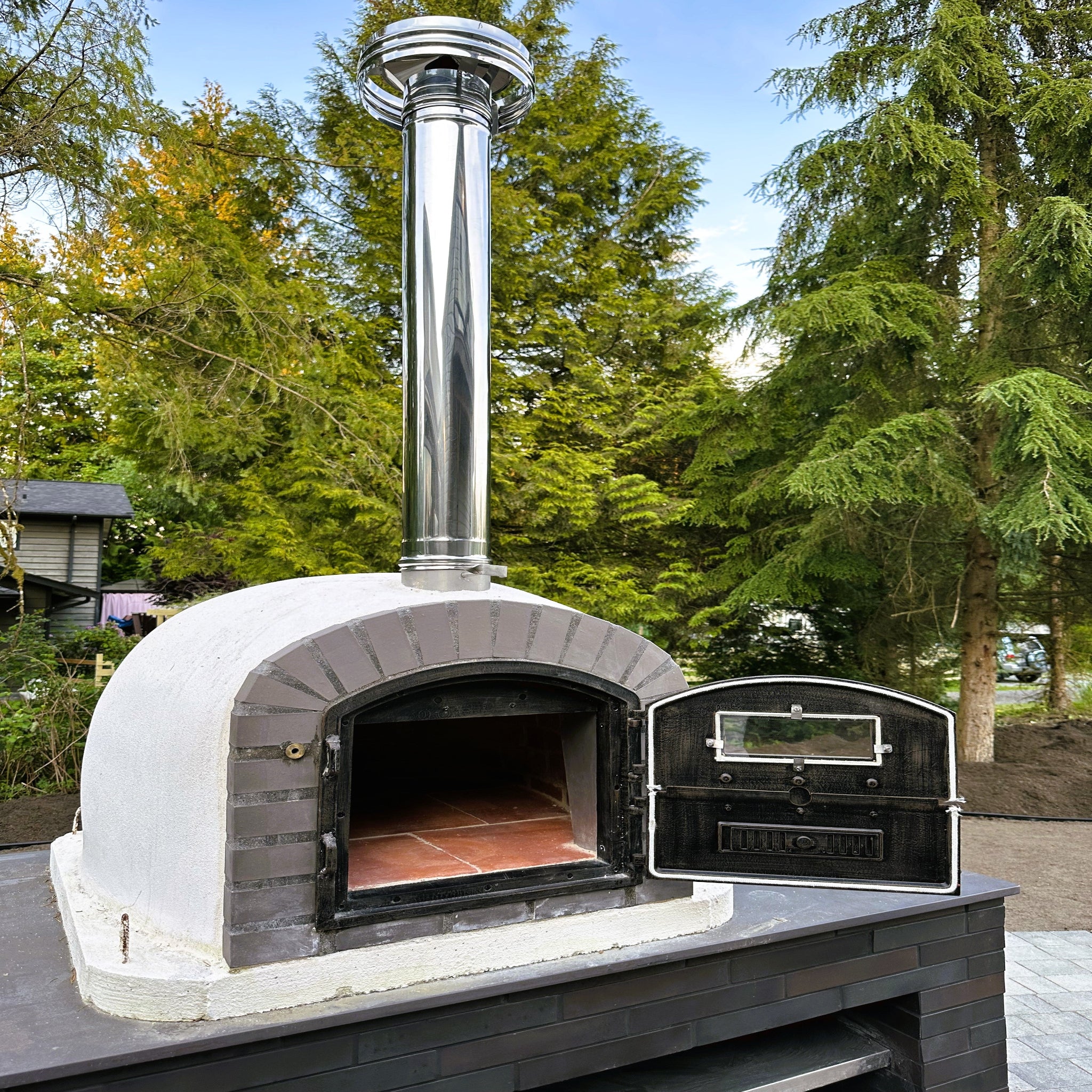 Outdoor brick pizza oven with chimney in a garden setting