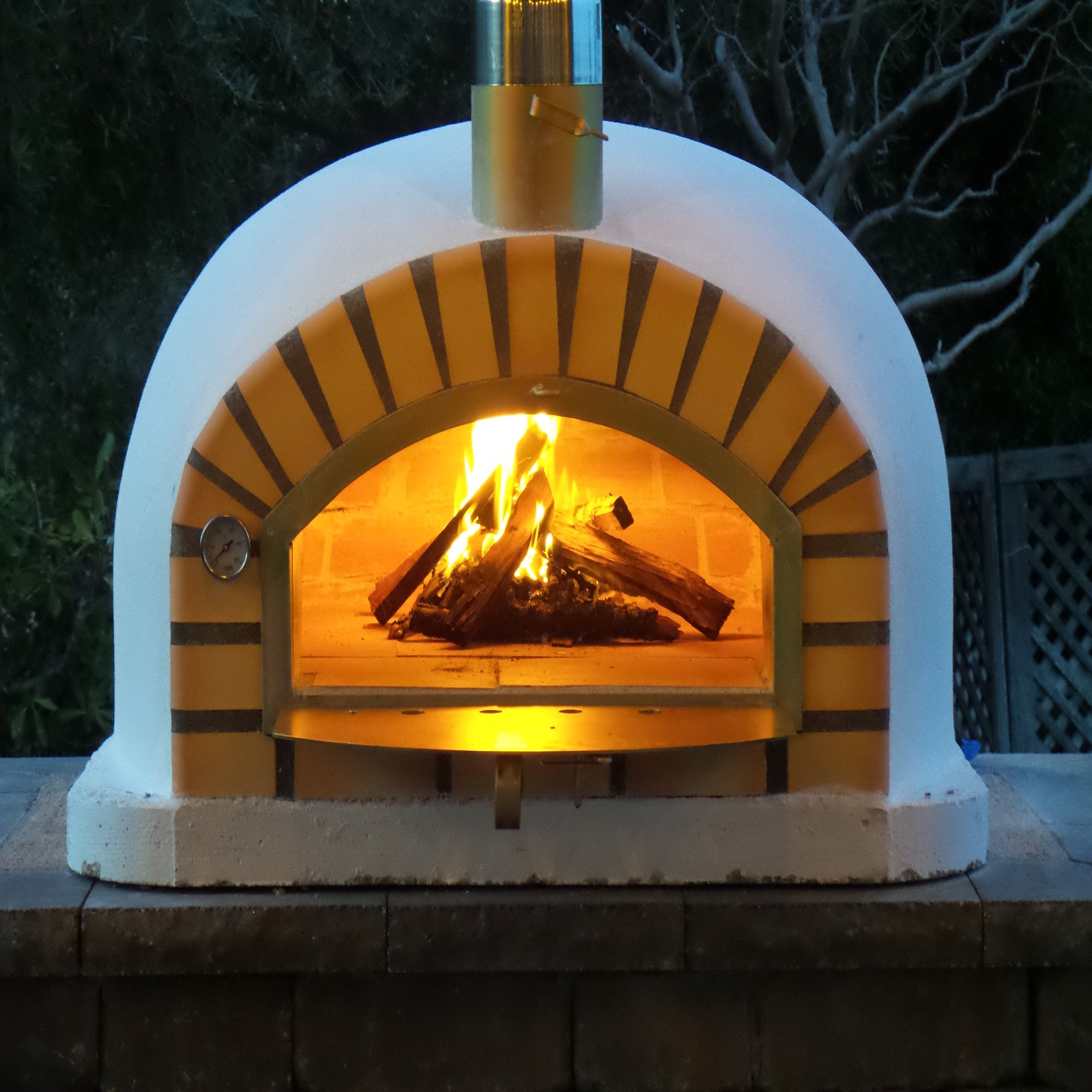 Wood-fired outdoor pizza oven with glowing interior and firewood inside, set against a dark background.