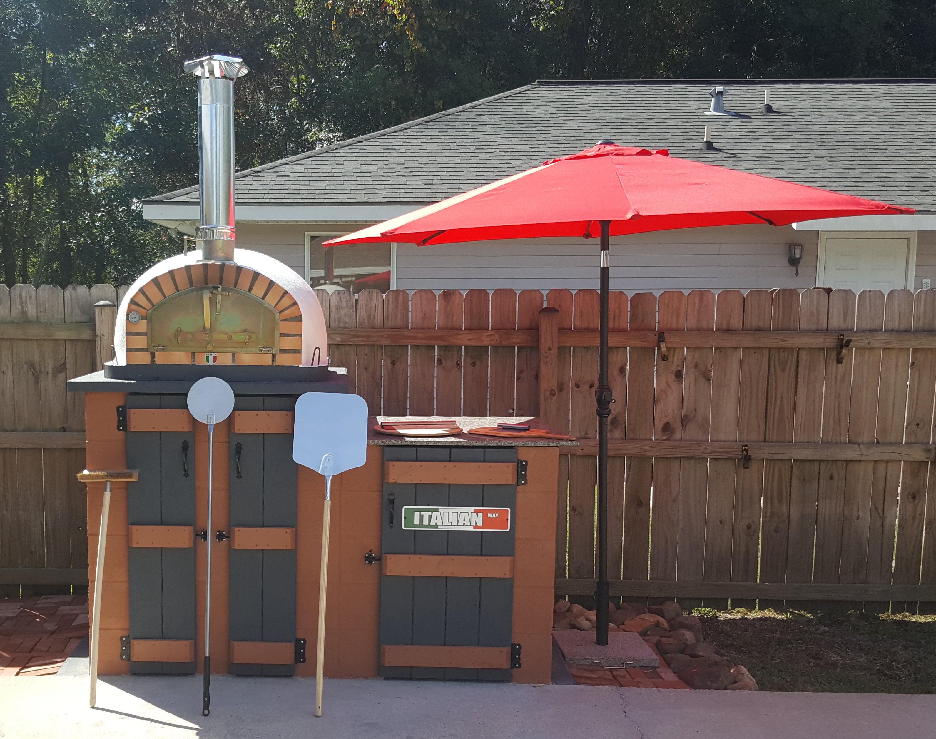Outdoor pizza oven with a red umbrella in a backyard setting