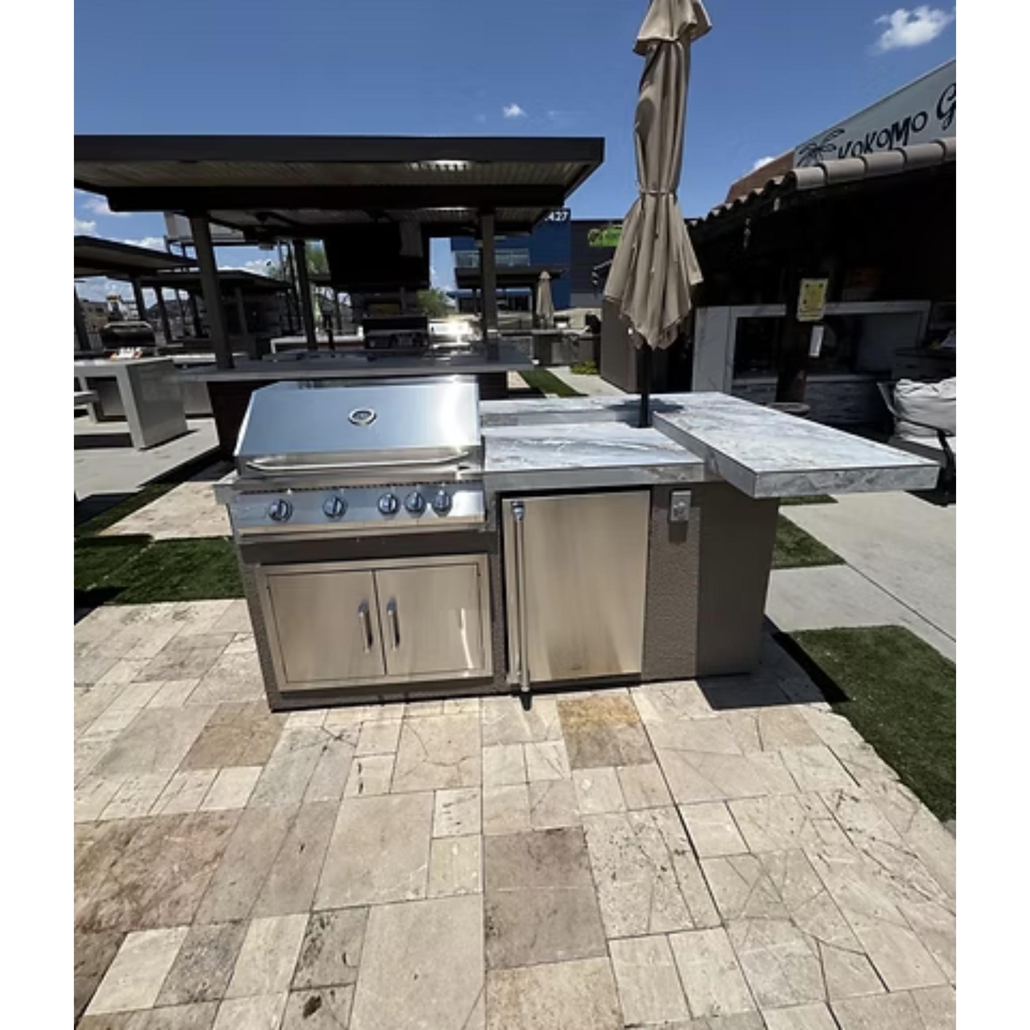 Outdoor kitchen with stainless steel grill and refrigerator on a stone patio